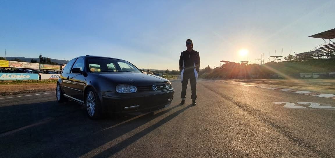 Golf negro en la pista al atardecer, junto a su piloto con buzo de carrera